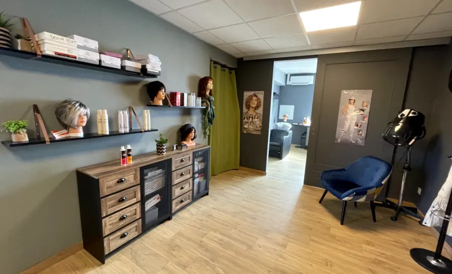 L’espace d’accueil avec un fauteuil, les perruques exposées et la porte ouverte sur une cabine