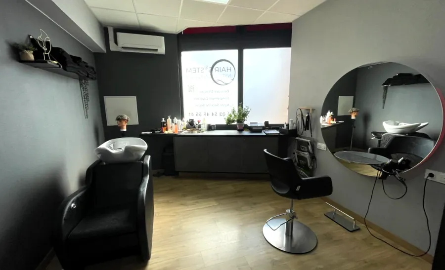 Une cabine privée : fauteuil face à un grand miroir rond, bac à shampoing, fenêtre dépolie