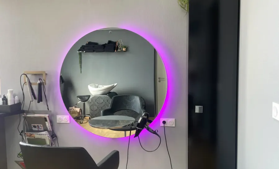 Le miroir rond éclairé d’une cabine, où l’on voit le bac à shampoing